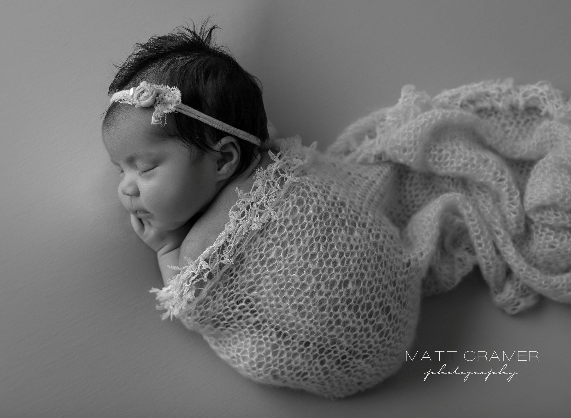 black and white aerial shot of curled up sleeping newborn baby on smooth fabric