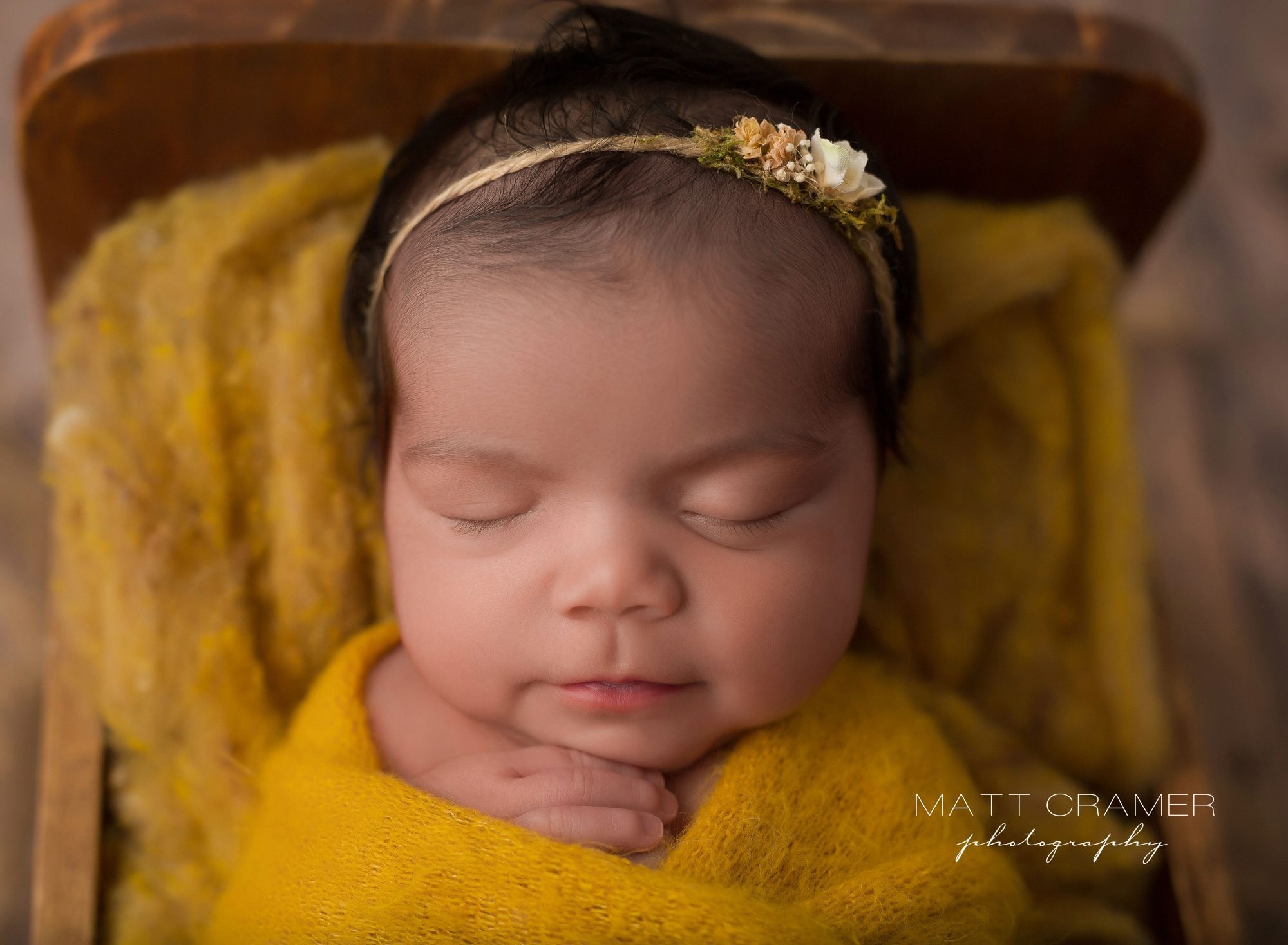 Newborn baby girl swaddled and wrapped in yellow fabric sleeping in wood baby bed photography prop during her Newborn Photography session in Los Angeles