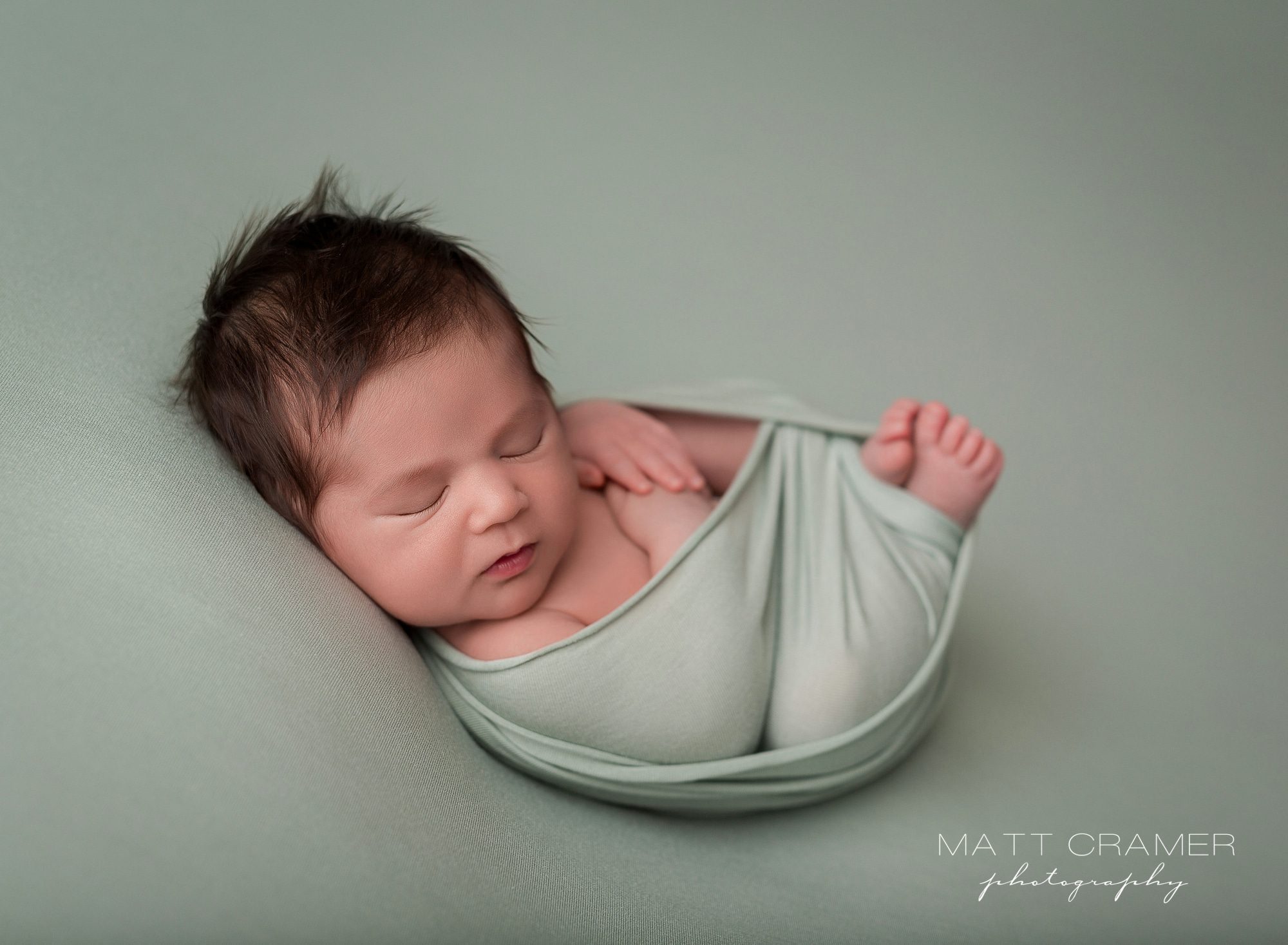 newborn baby posed on sage fabric