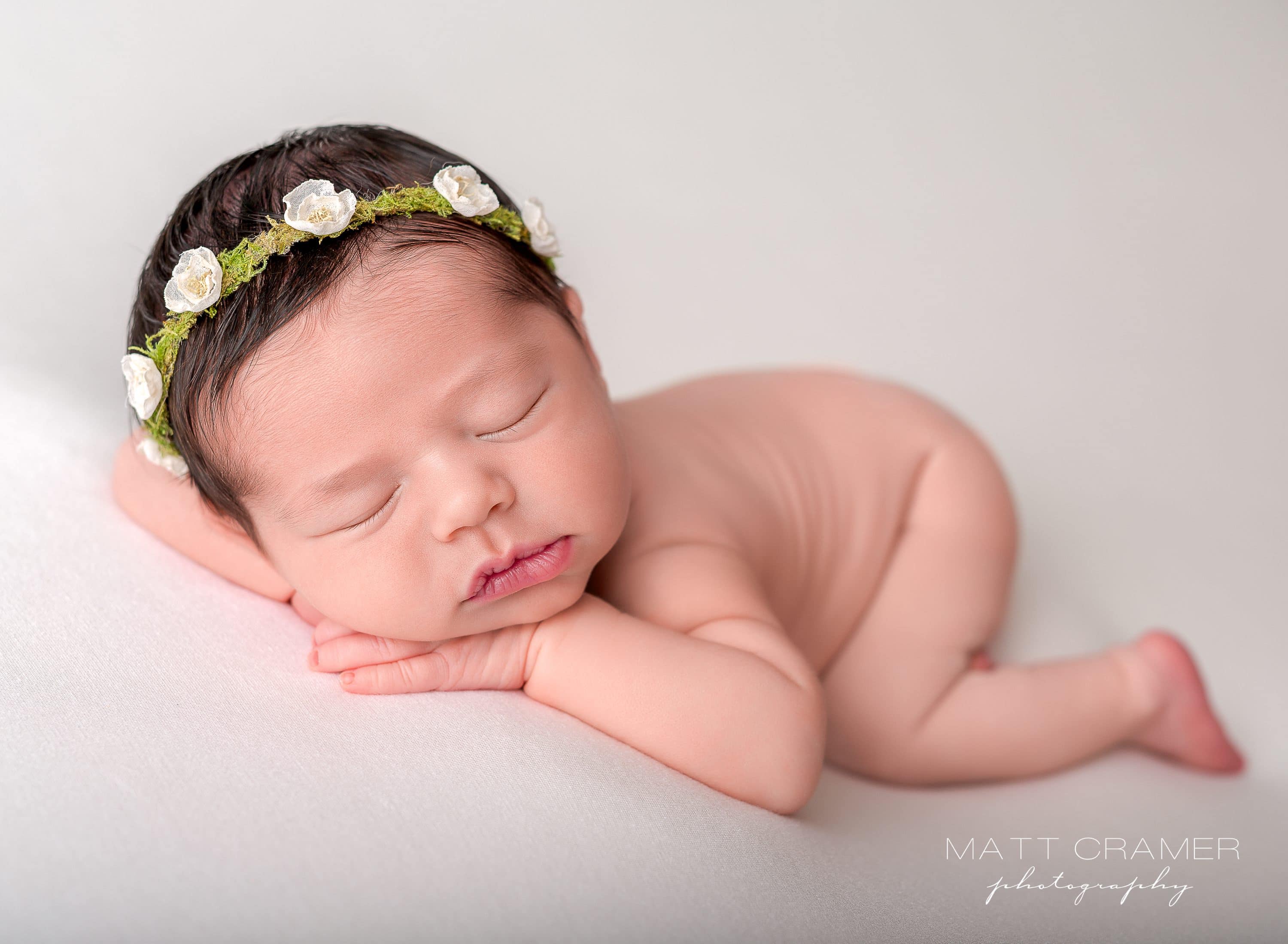 newborn baby poses with her face resting on her hands