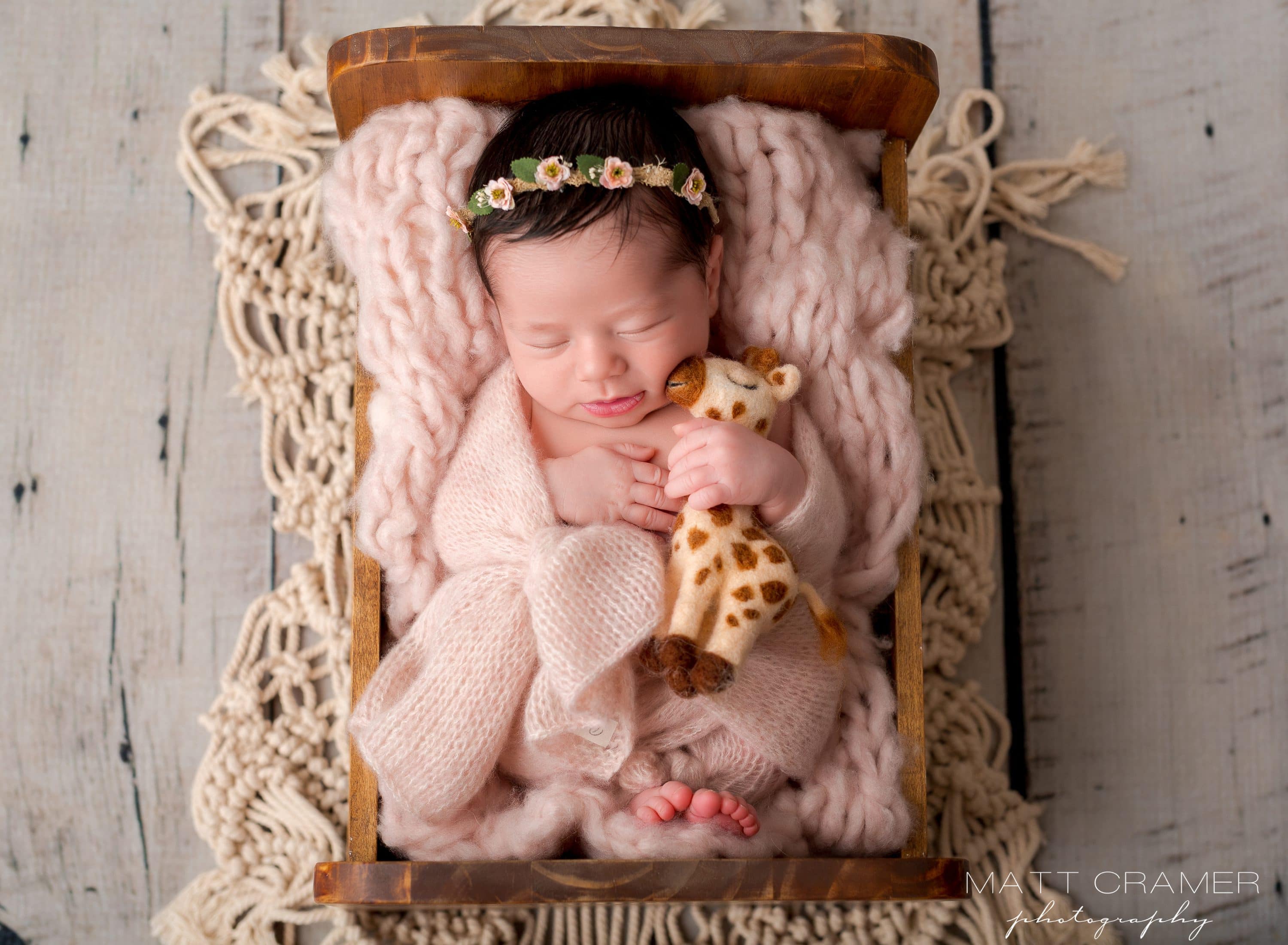 infant girl laying in wood baby bed prop with felted giraffe toy