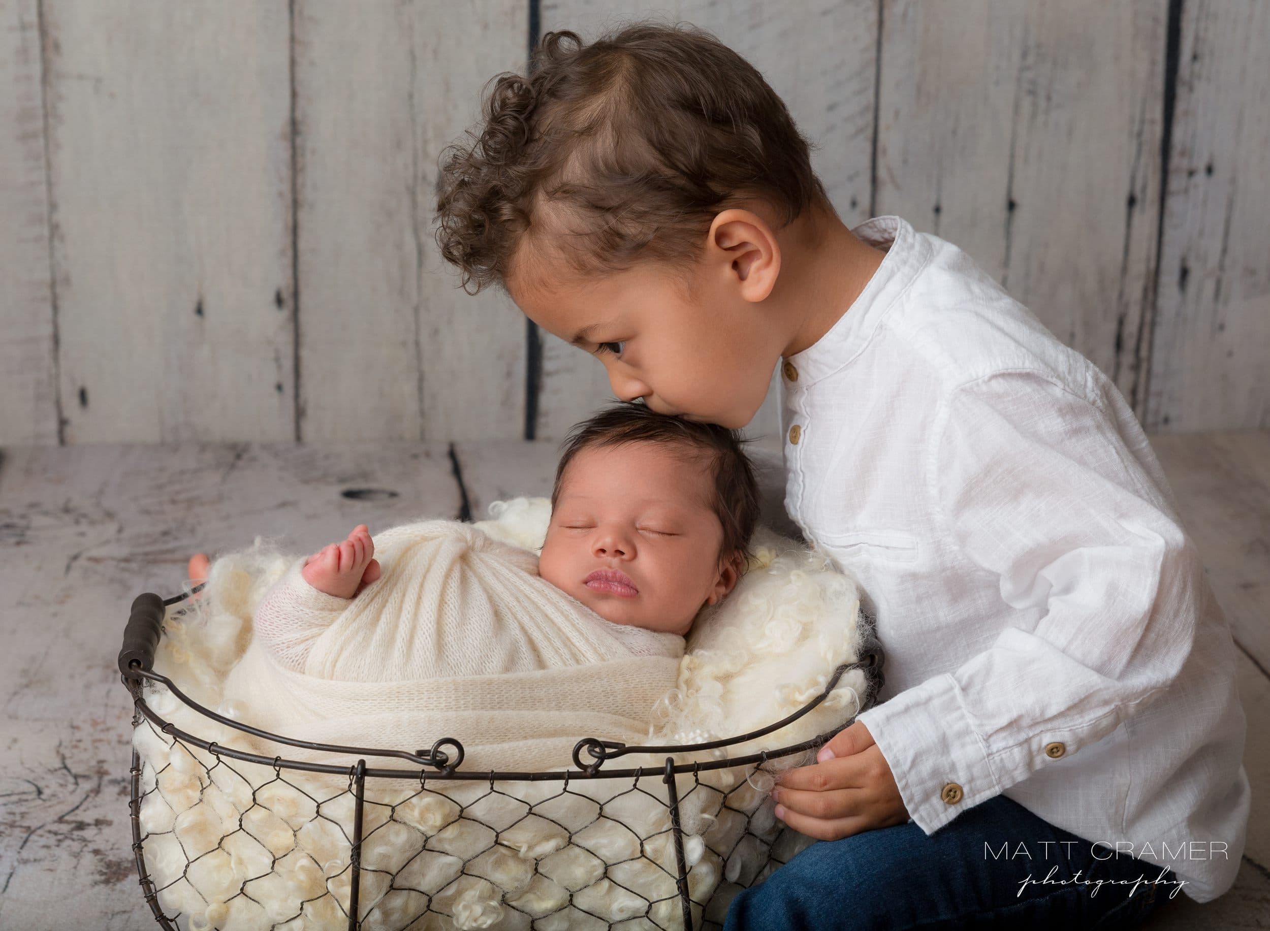 Toddler sibling kissing baby newborn brother