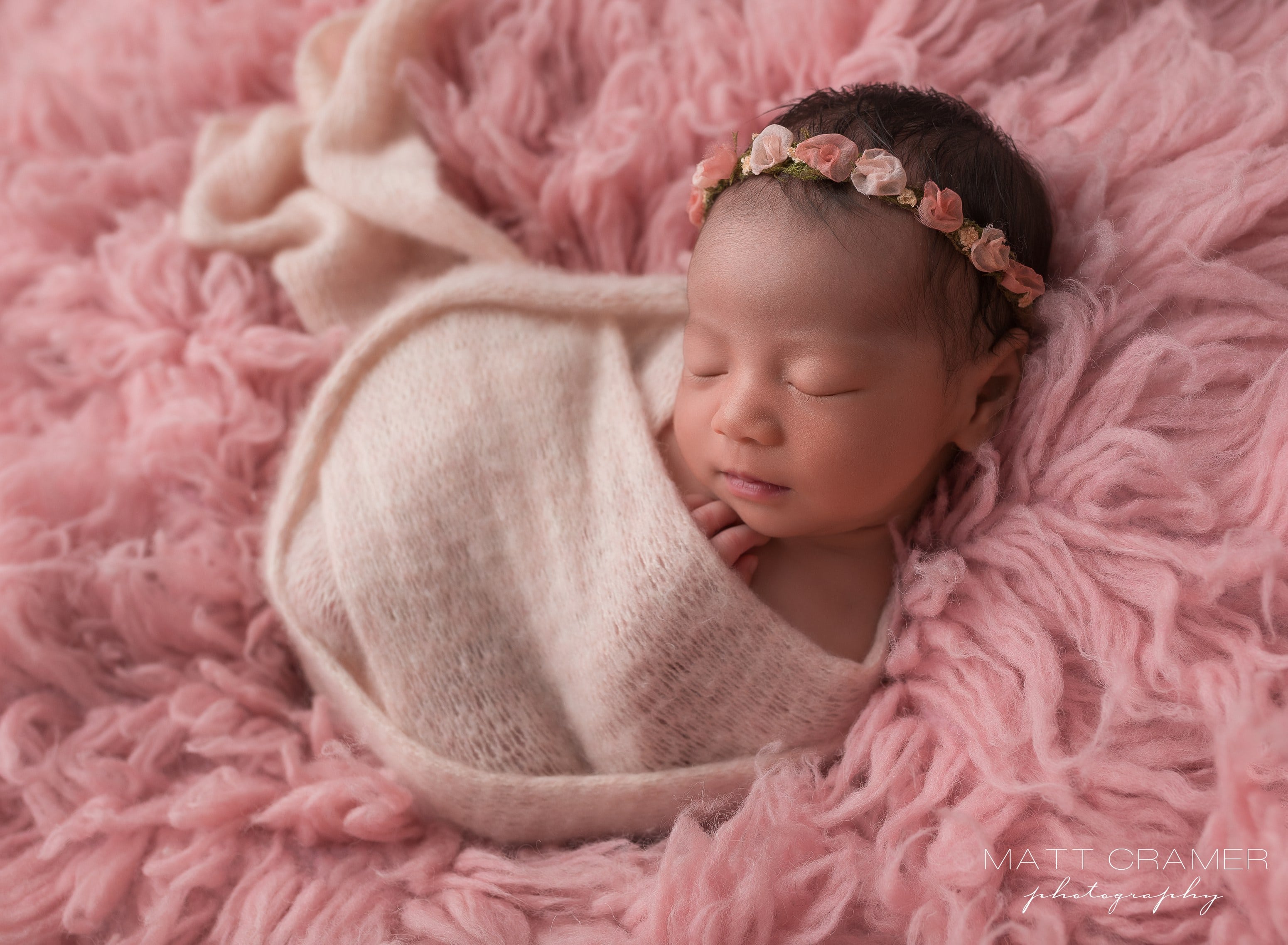 newborn baby in a light pink swaddle, laying on pink textured background during a newborn photography session