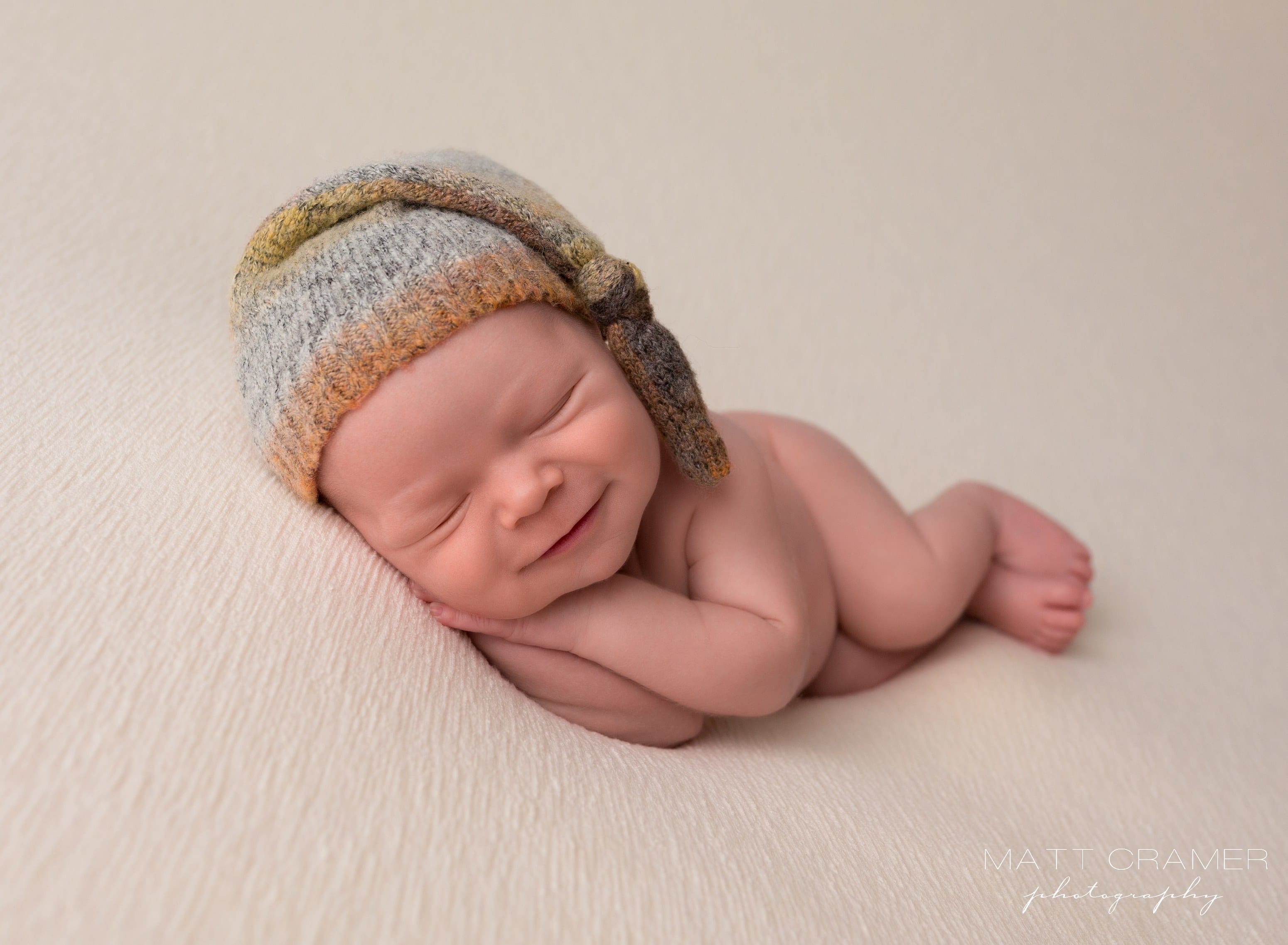 smiling baby boy with hat on laying on his side during a newborn photo shoot