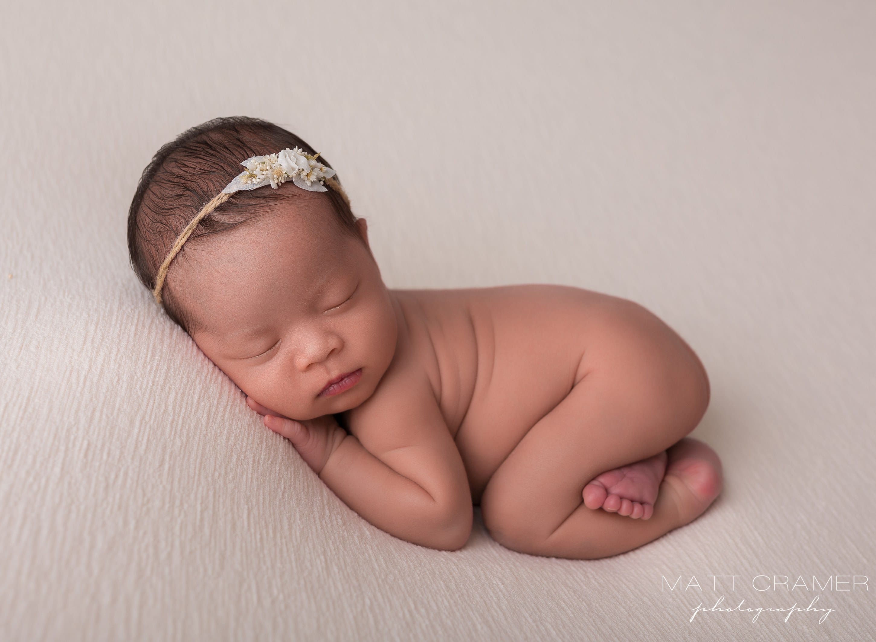 baby girl posed on cream fabric in professional newborn photography photoshoot