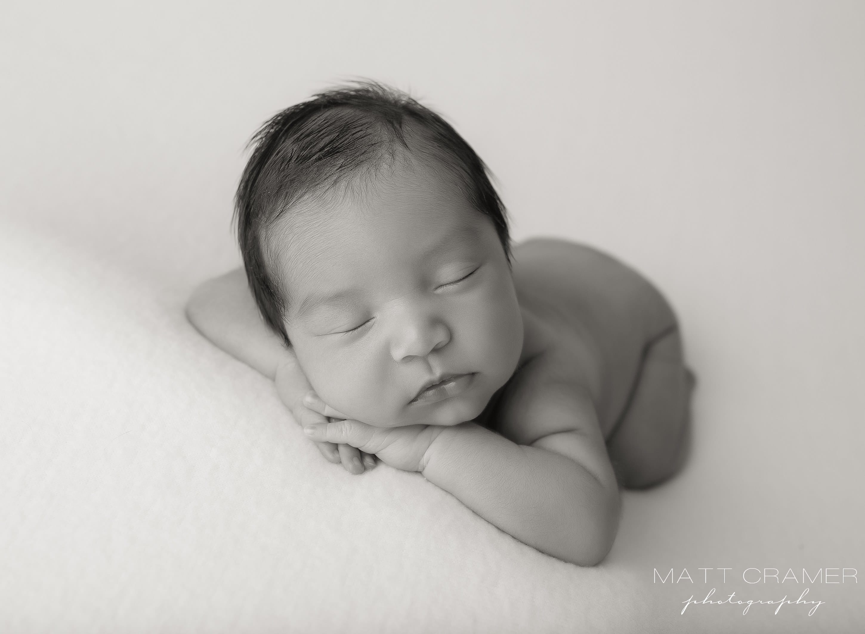 black and white photo of baby boy posed on solid fabric during a newborn photo shoot