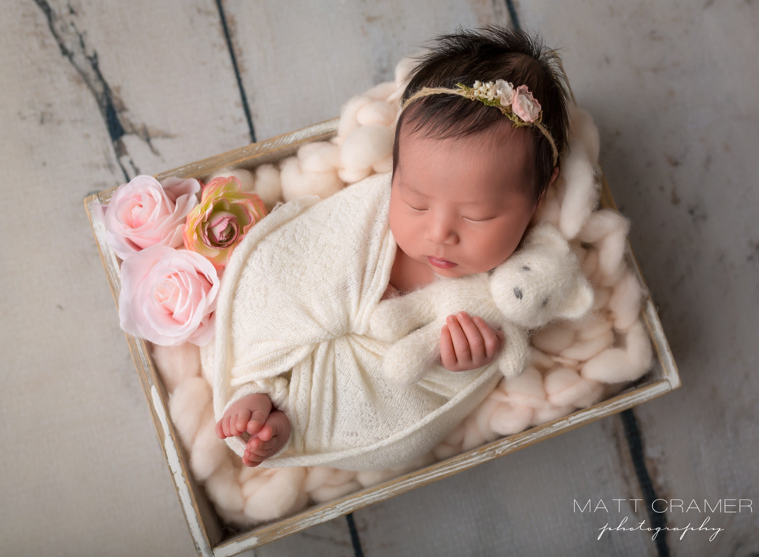 baby girl posed in white crate with pink flowers holding teddy bear