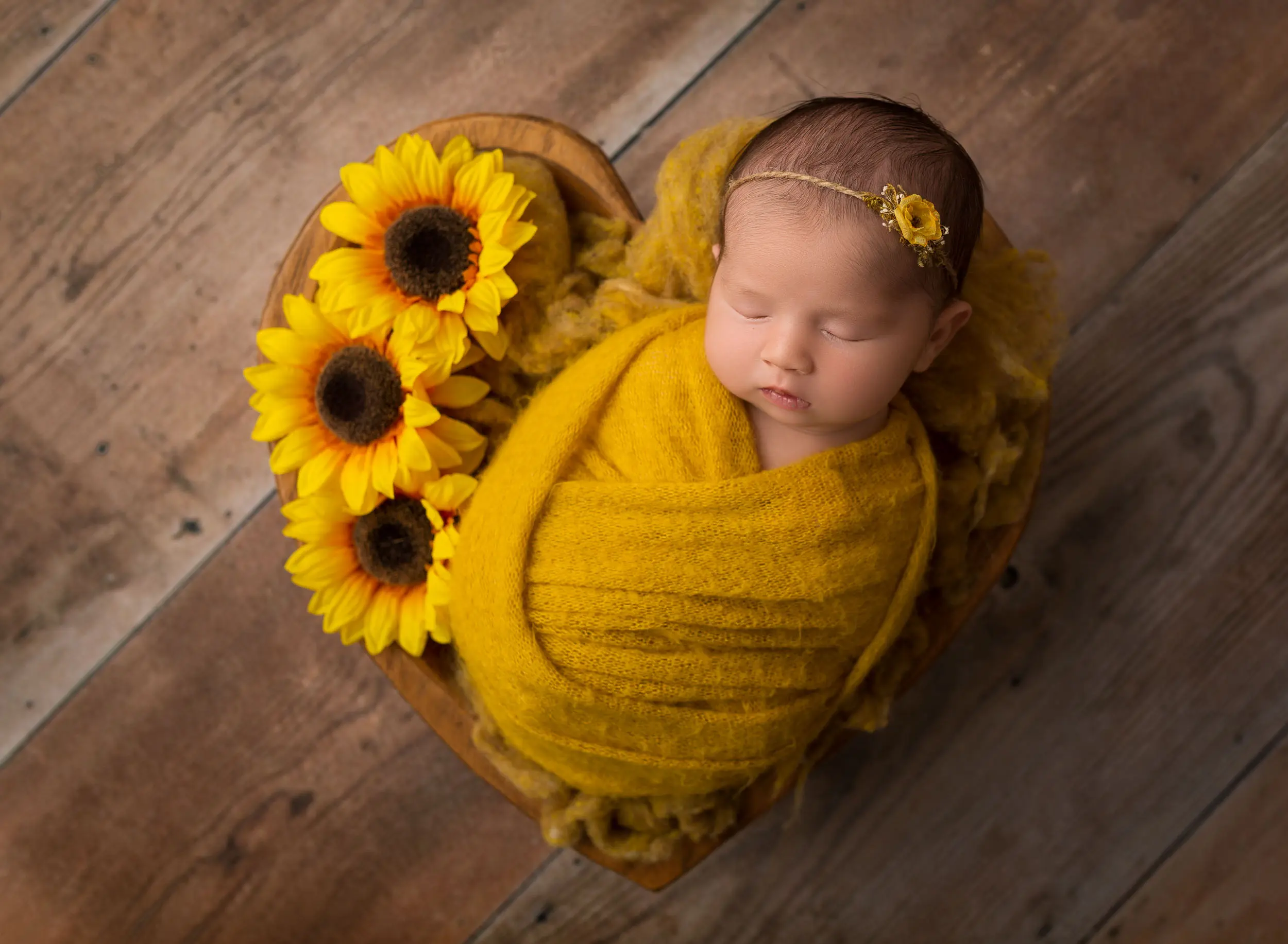 baby girl in newborn photography scene using yellow wrap and three sunflowers nestled next to baby