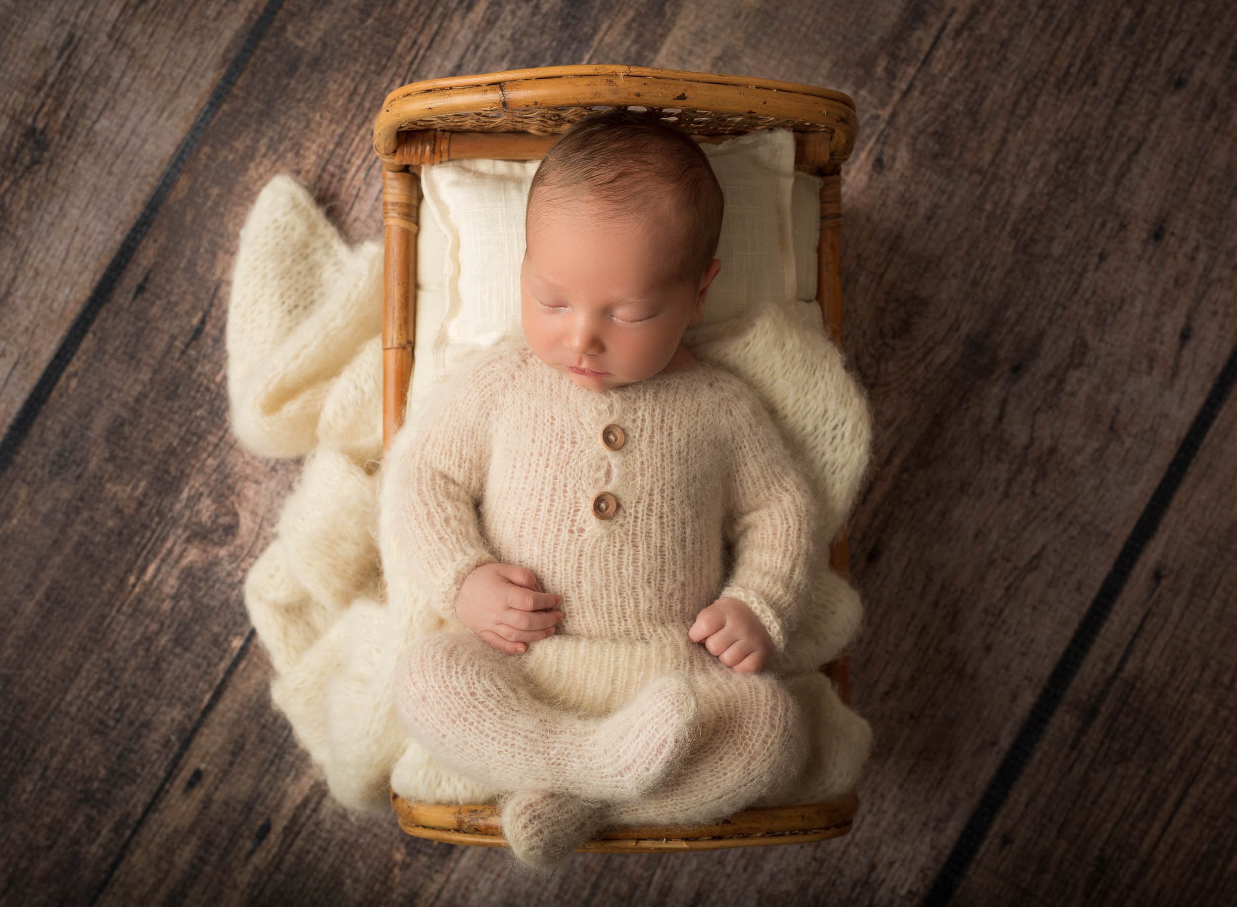 newborn boy in knit outfit laying on his back in baby bed