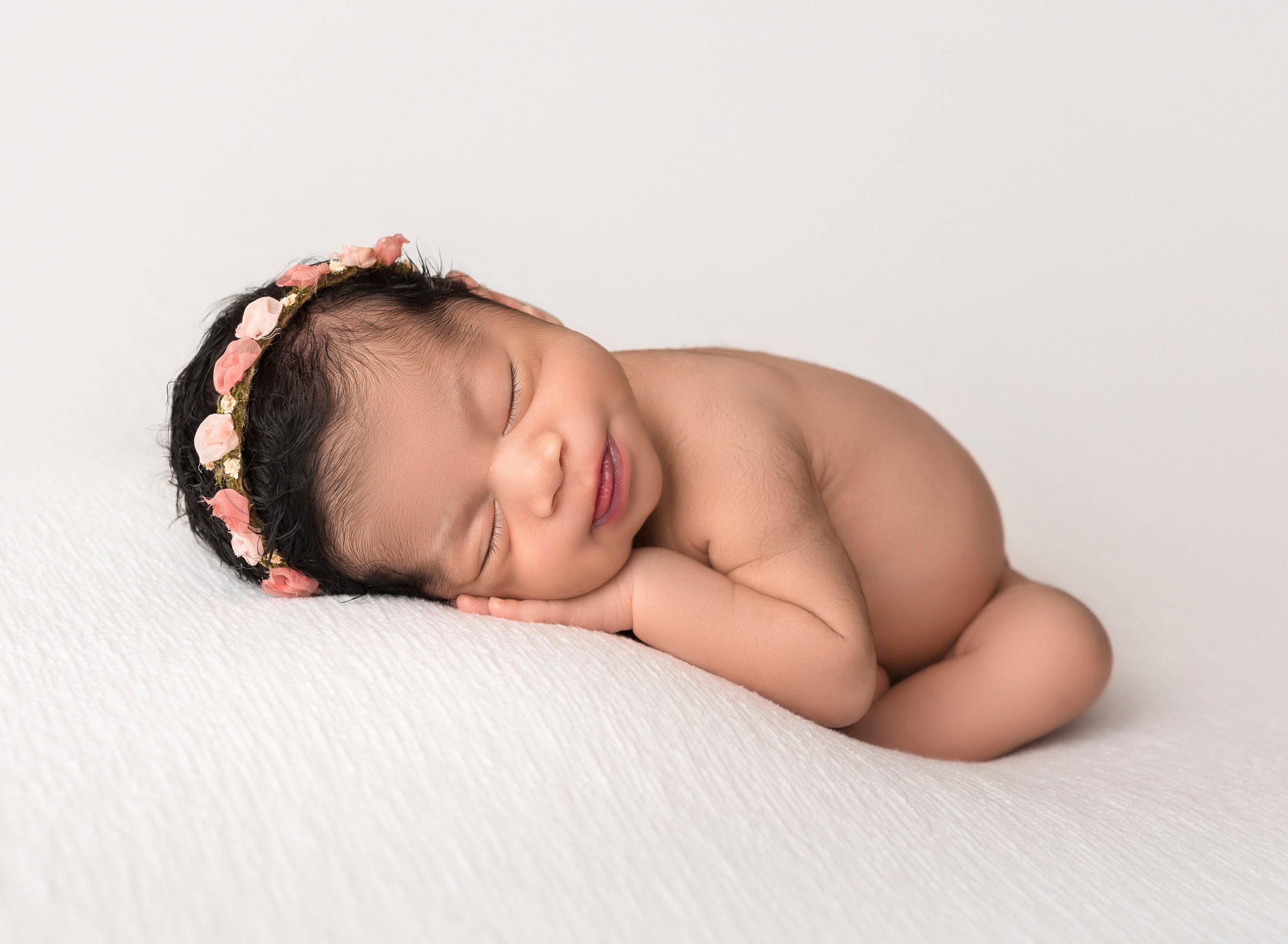 baby girl laying on white fabric in newborn photography pose