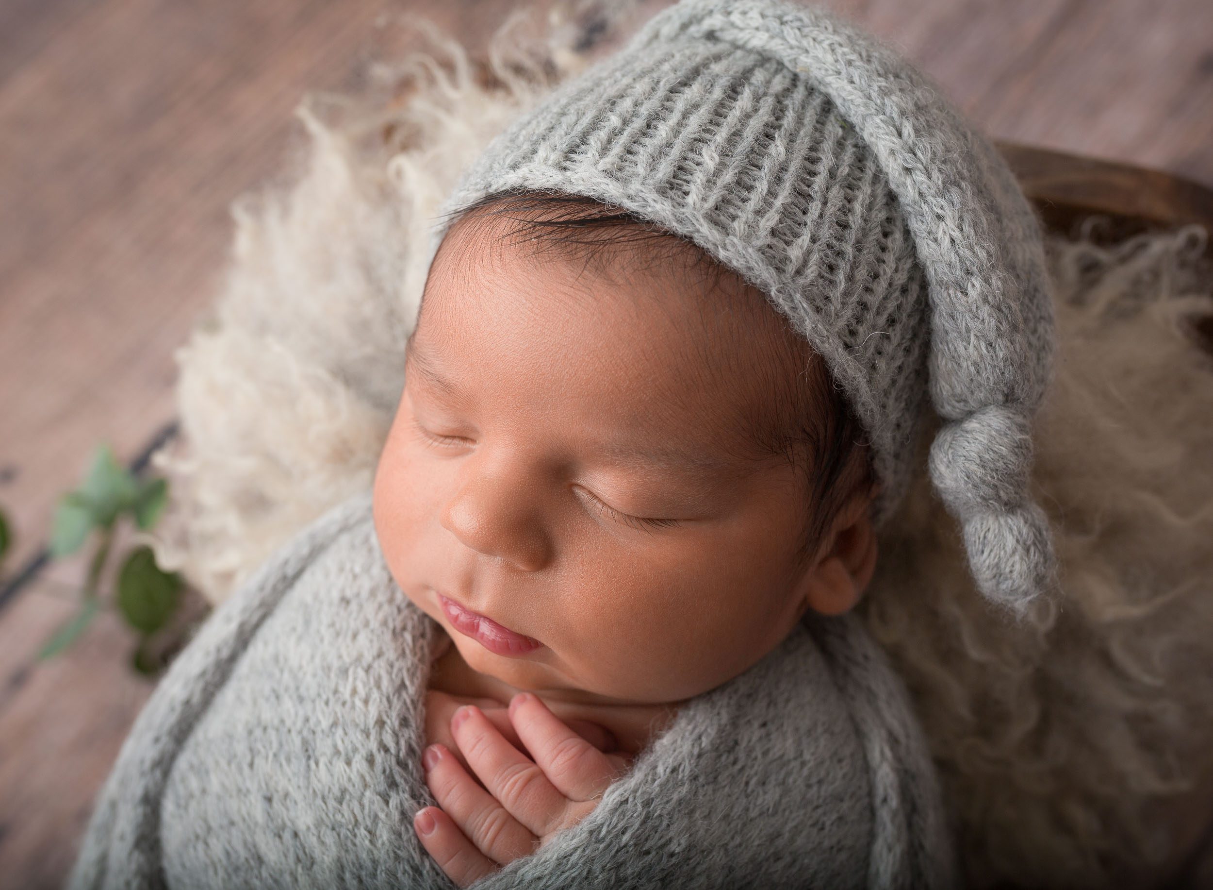infant boy wearing sleepy hat swaddled up