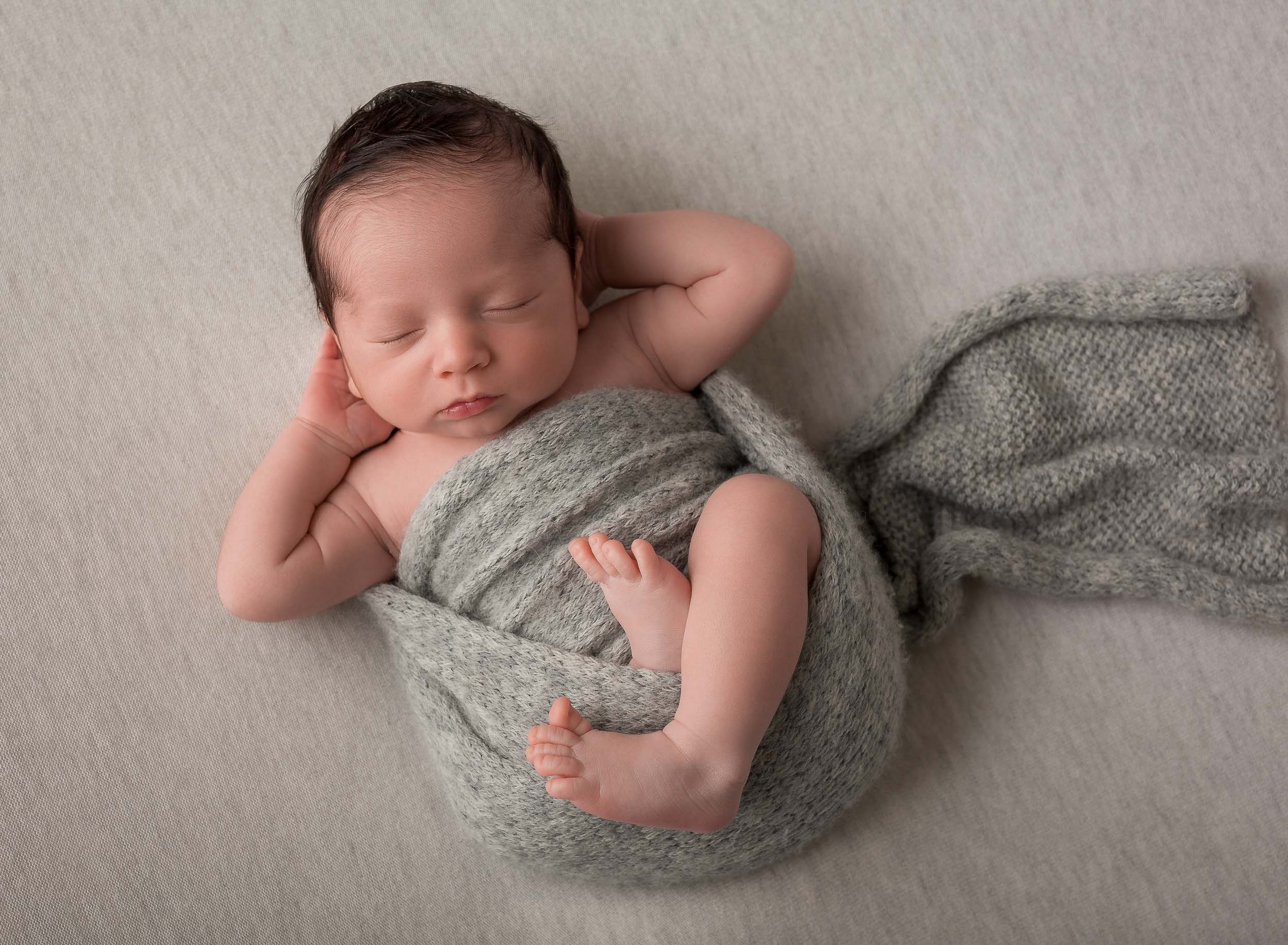 infant boy laying down with hands behind his head