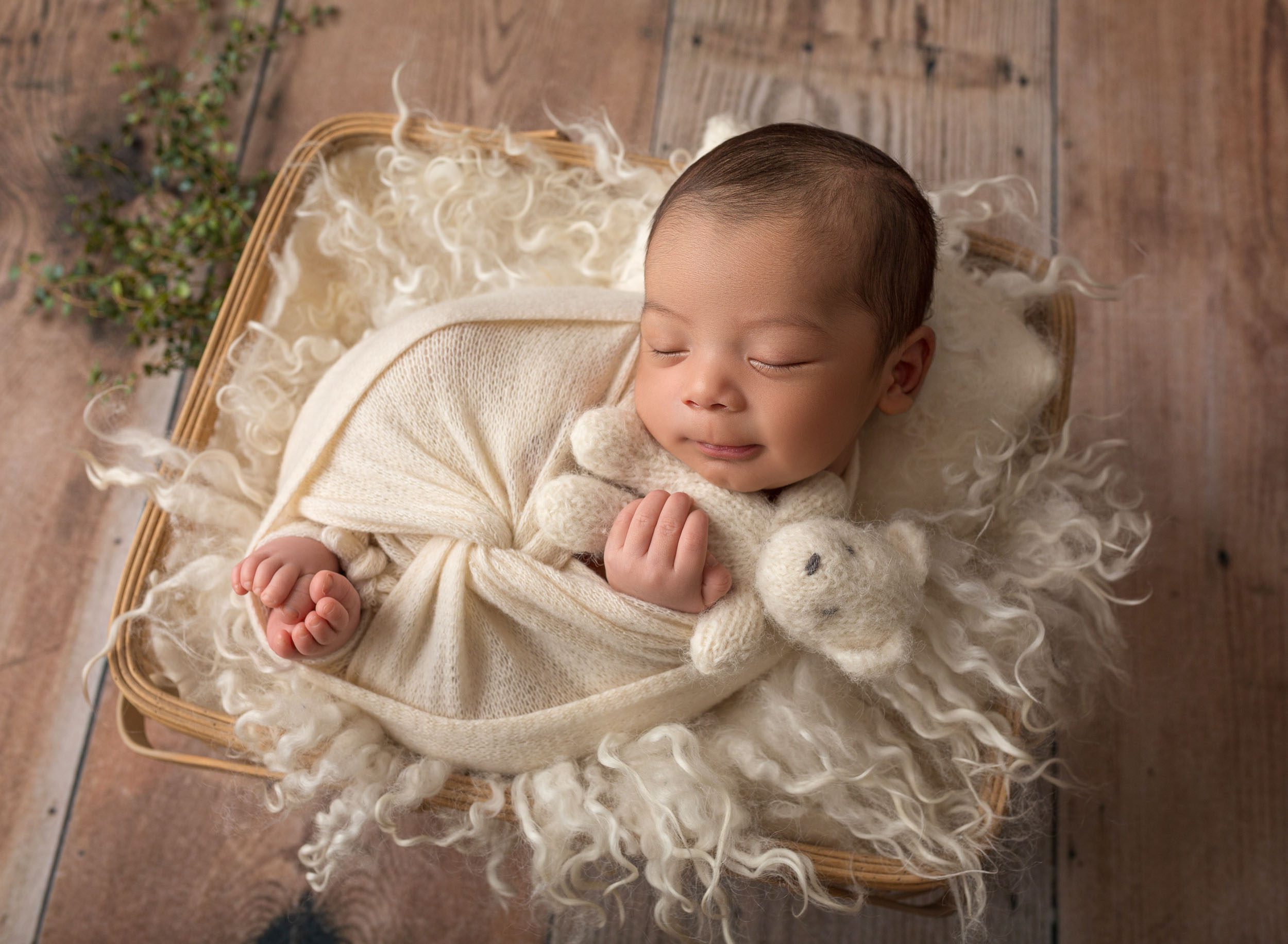 baby boy swaddled in white, snuggling teddy bear in basket