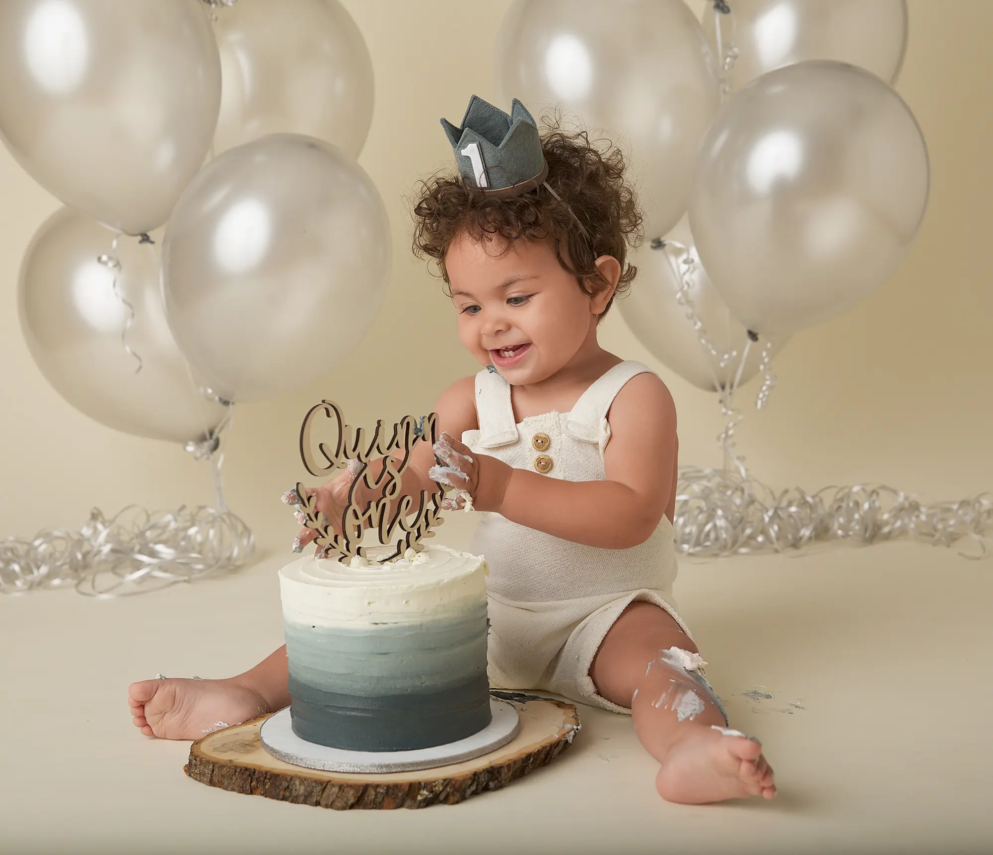 baby boy sitting in front of balloons eating cake