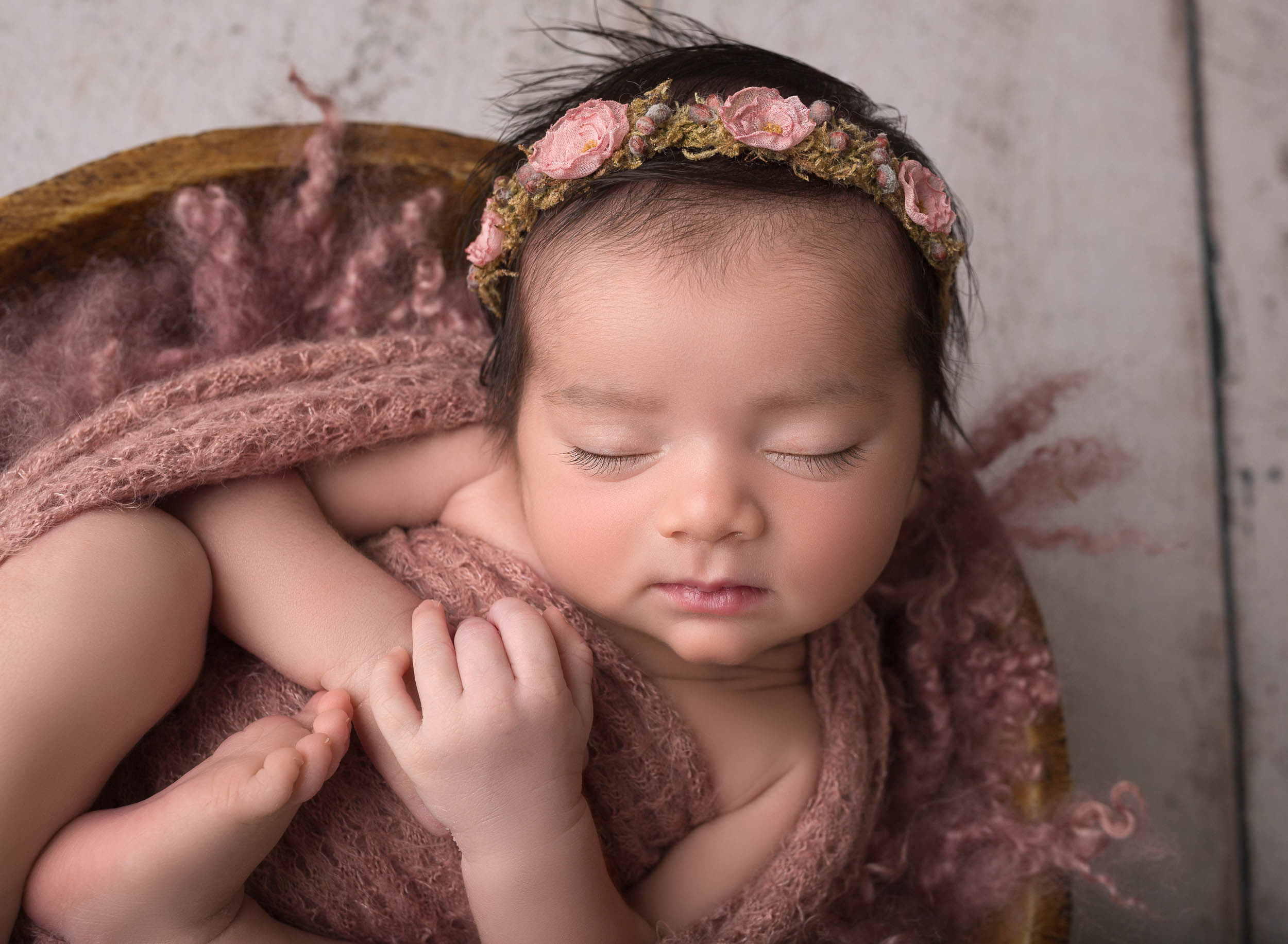 newborn baby girl wearing pink floral headband swaddled in pink wrap