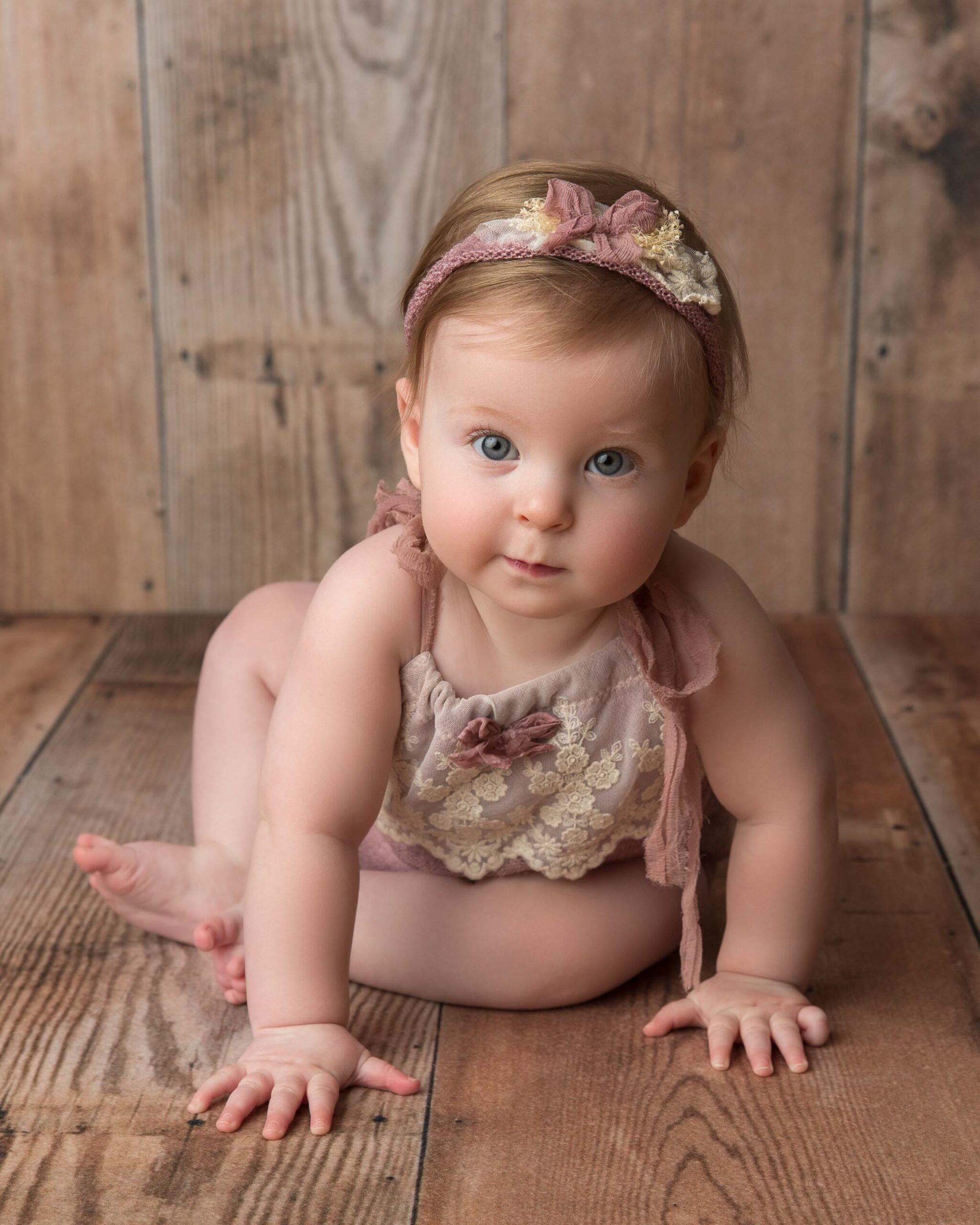 baby girl sitting on wood background leaning forward on her knees