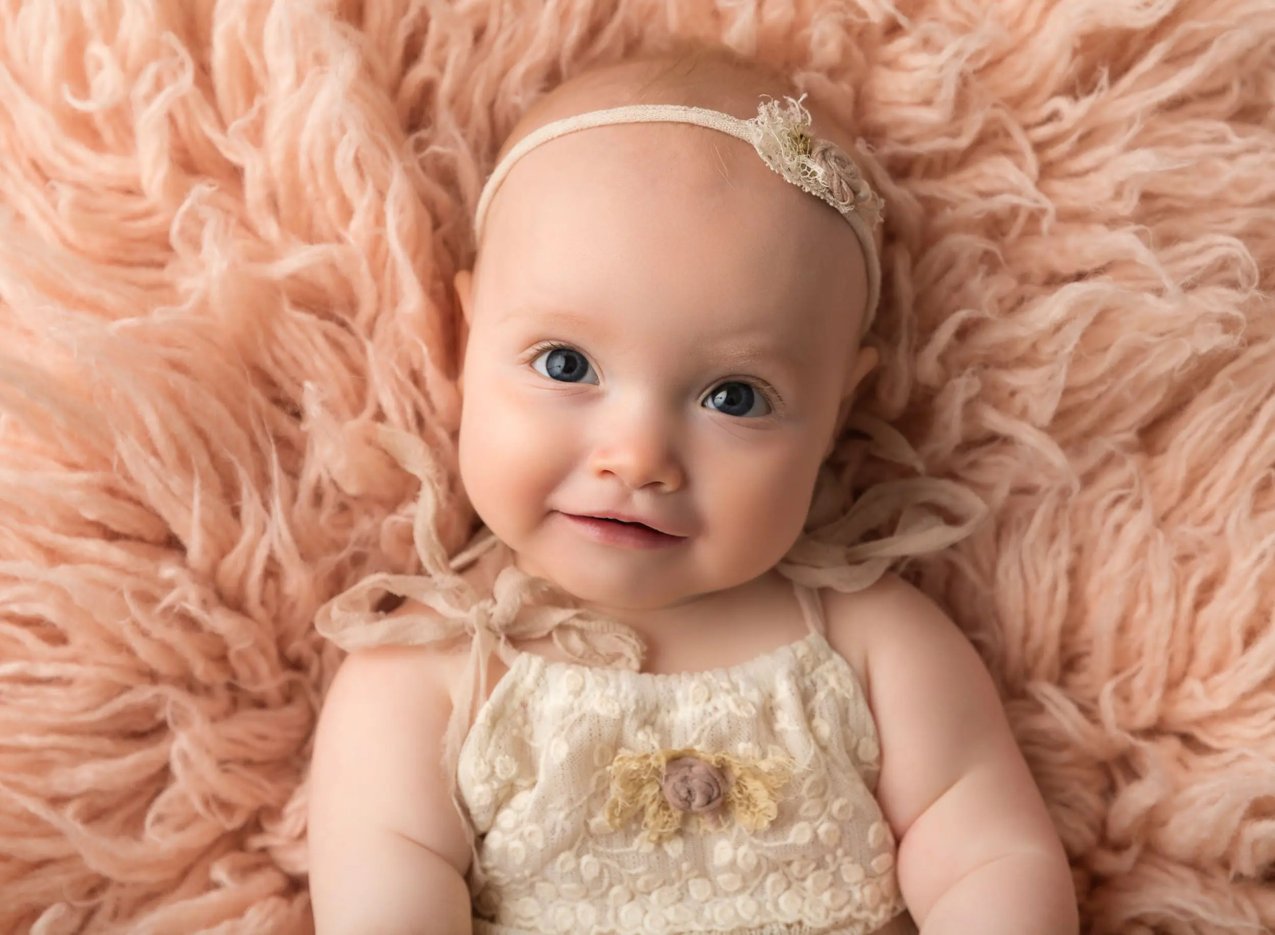 baby girl looking up at camera laying on blush colored rug