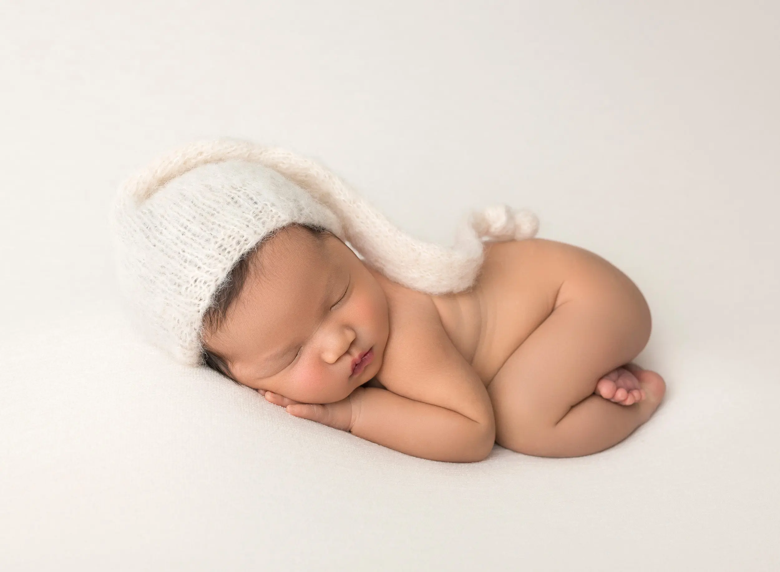 baby girl sleeping on tummy with cream hat on
