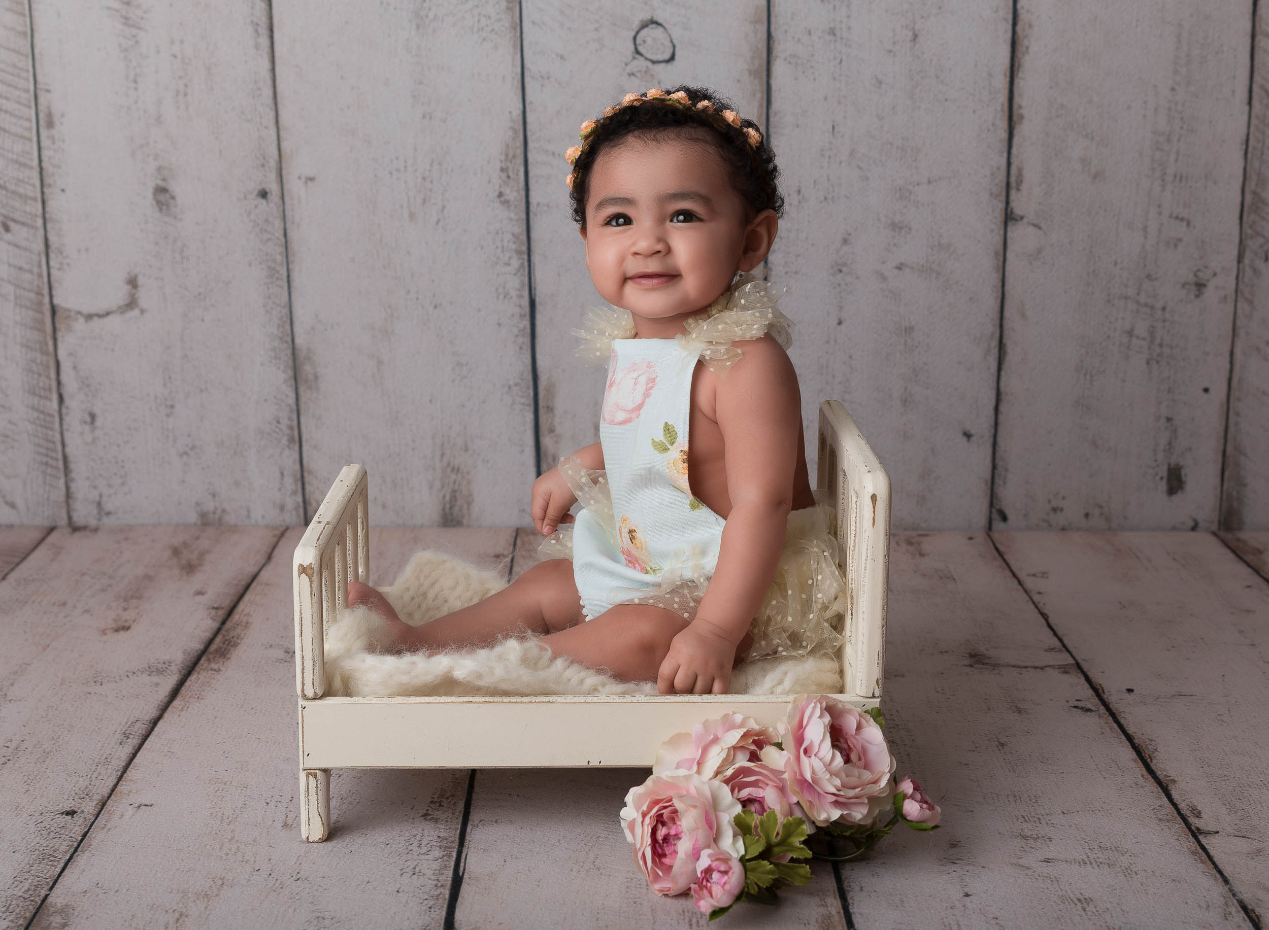 baby girl sitting on photo prop bed in girly outfit