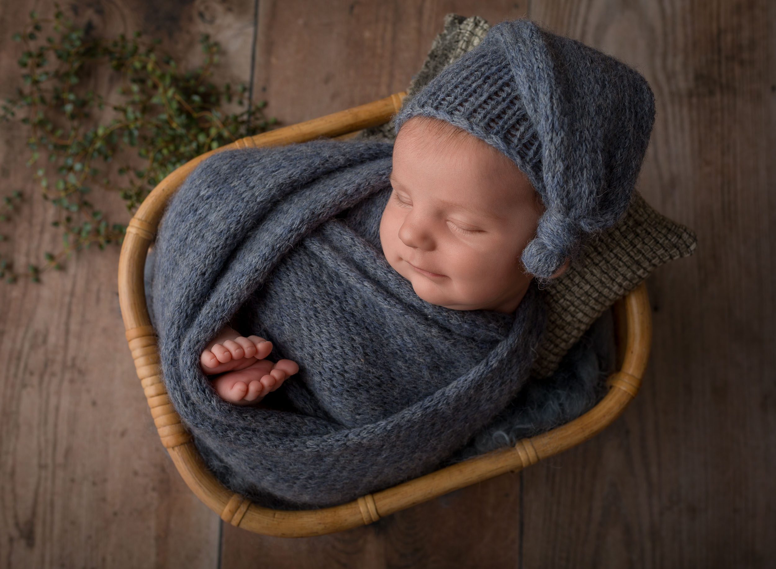 new born baby boy wrapped in blue wearing knit hat in basket