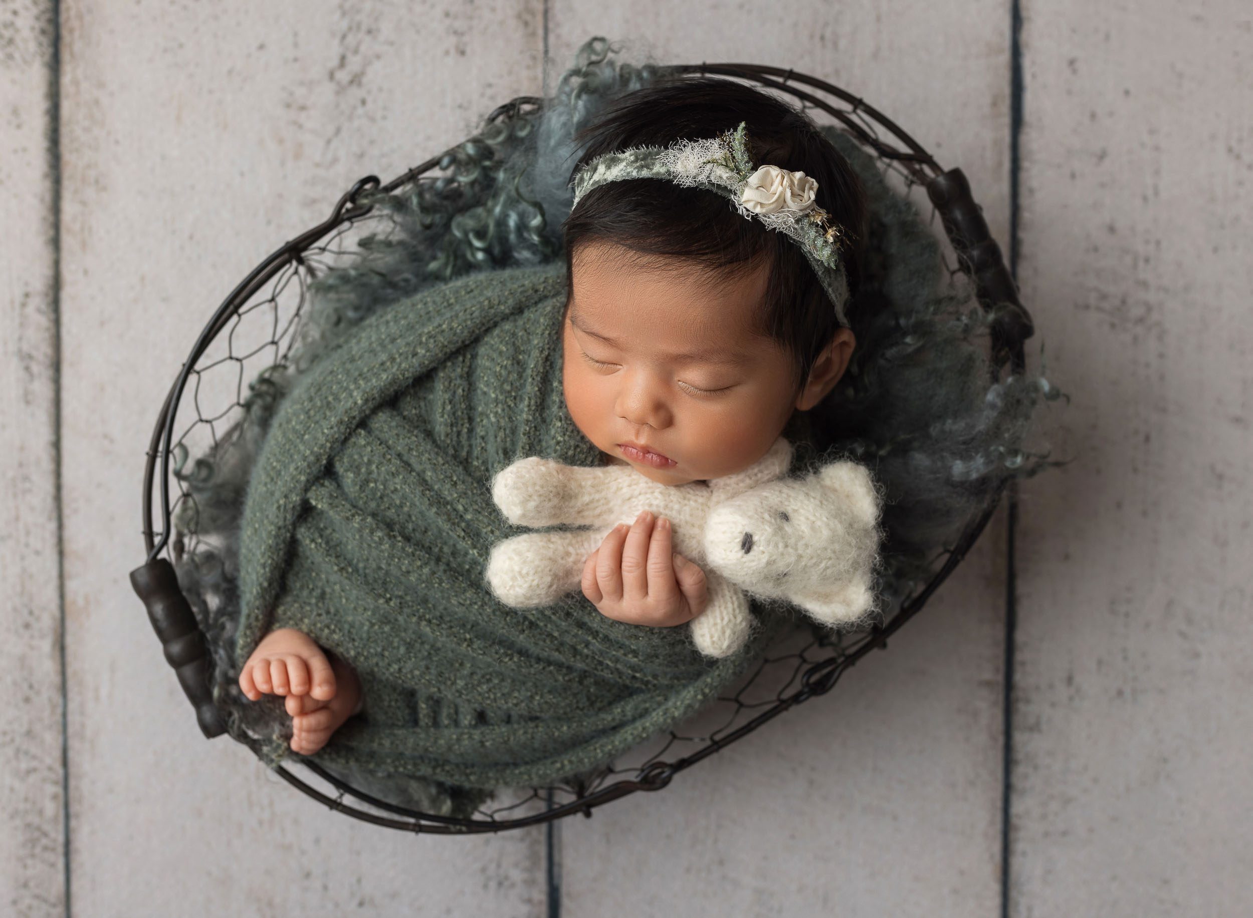 baby girl swaddled in green snuggling white teddy bear