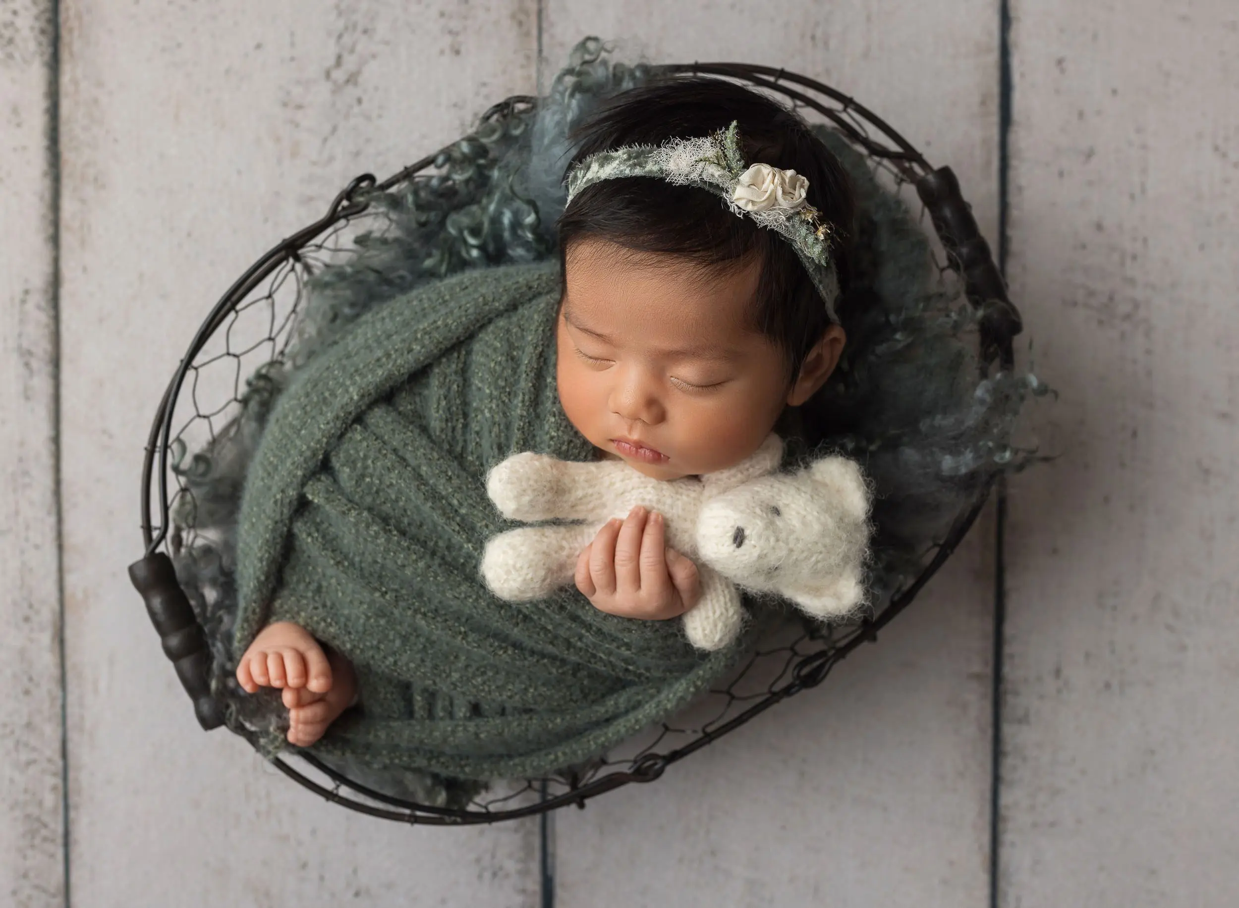 baby girl swaddled in green snuggling white teddy bear